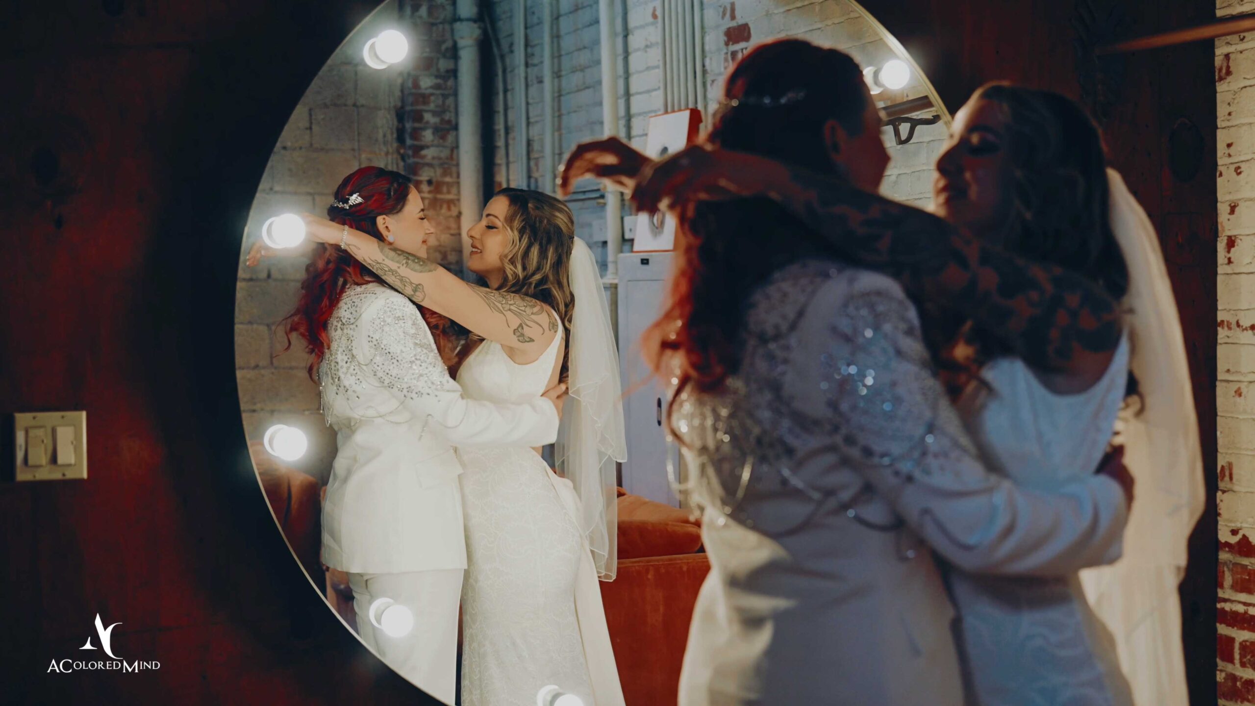 Two brides embracing while getting ready for their LGBTQ wedding at The Millwick in Los Angeles, reflected in a cinematic vanity mirror.