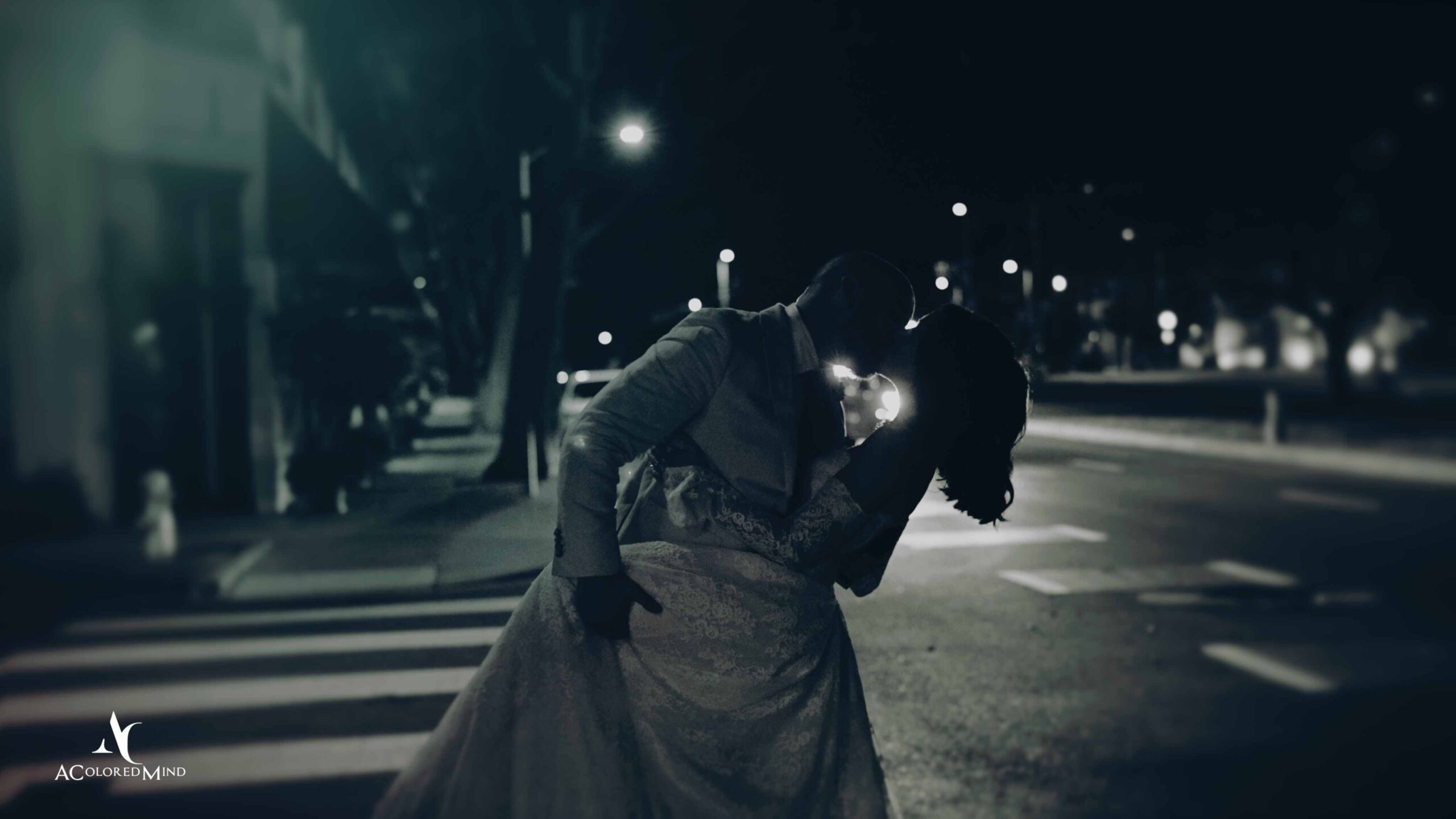 Cinematic nighttime wedding portrait of a couple kissing on a quiet city street.