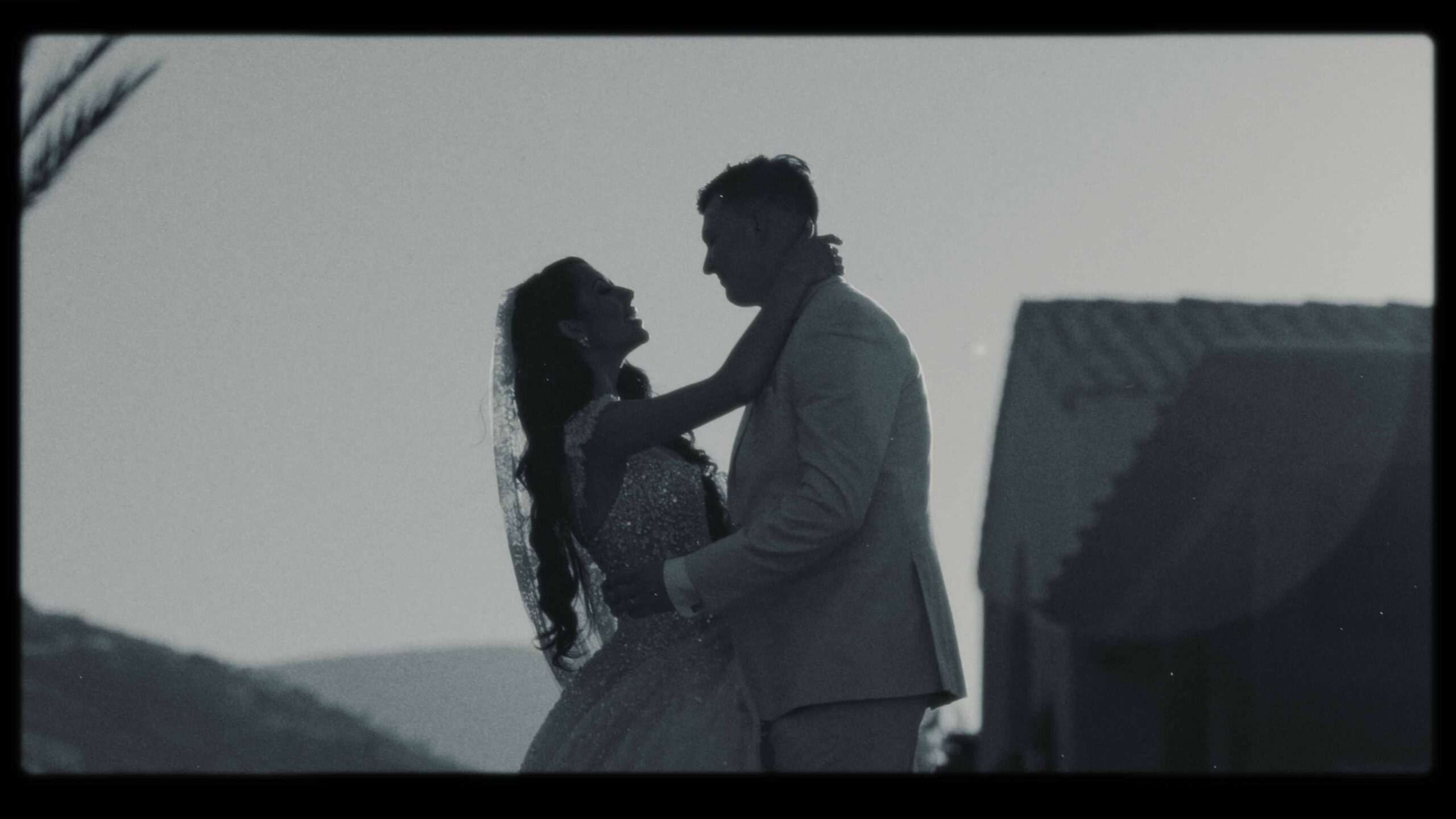A cinematic black and white silhouette of a bride and groom embracing and smiling at their wedding.